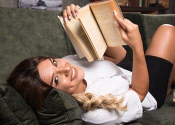 Mulher sorridente deitada no sofá lendo um livro — como transformar a leitura em hábito com passo a passo fácil para quem vive ocupado