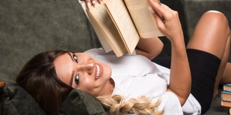 Mulher sorridente deitada no sofá lendo um livro — como transformar a leitura em hábito com passo a passo fácil para quem vive ocupado