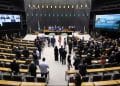 Vista panorâmica do plenário da Câmara dos Deputados em Brasília, com parlamentares ocupando as bancadas e grandes telas de votação exibindo informações sobre os projetos em pauta.