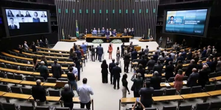 Vista panorâmica do plenário da Câmara dos Deputados em Brasília, com parlamentares ocupando as bancadas e grandes telas de votação exibindo informações sobre os projetos em pauta.