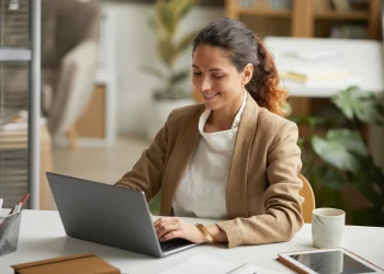 Profissional trabalhando no laptop em escritório moderno, representando os desafios e barreiras enfrentados por mulheres no crescimento da carreira.