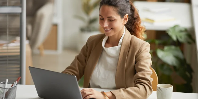 Profissional trabalhando no laptop em escritório moderno, representando os desafios e barreiras enfrentados por mulheres no crescimento da carreira.