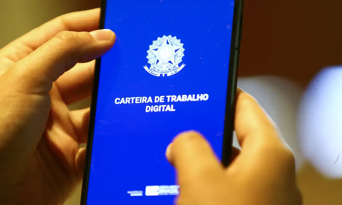 Mãos segurando celular com a tela do aplicativo Carteira de Trabalho Digital aberta — documento obrigatório para trabalhadores formais no Brasil em 2026