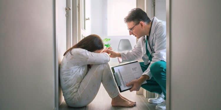 Médico acolhendo mulher que chora sentada no chão, demonstrando empatia e cuidado com a saúde emocional