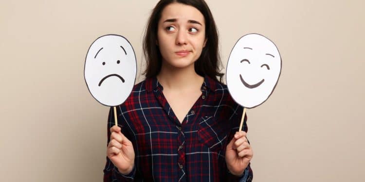 Jovem segurando duas máscaras com expressões de tristeza e felicidade simbolizando o controle das emoções.