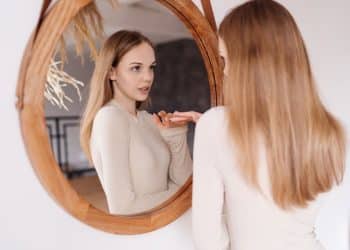 Jovem observando o próprio reflexo no espelho em representação do desenvolvimento da autoestima feminina.