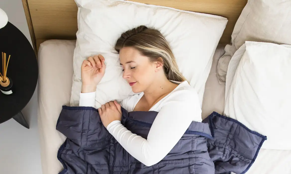 Mulher dormindo tranquilamente em uma cama com travesseiro branco e cobertor azul, representando o descanso mental e o sono de qualidade