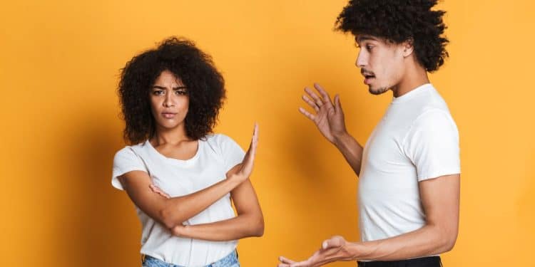 Fotografia de um homem e uma mulher sobre fundo amarelo. A mulher, à esquerda, tem os braços cruzados e uma mão estendida em sinal de "pare", com expressão séria. O homem, à direita, gesticula como se estivesse dando uma explicação ou conselho.