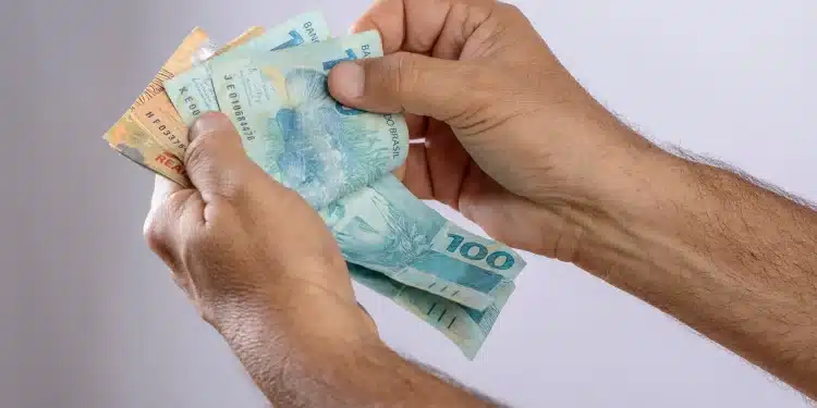 Pessoa segurando notas de real enquanto confere valores do benefício Pé-de-Meia de mil reais.