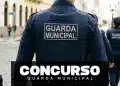 Imagem vertical mostrando as costas de um uniforme de Guarda Municipal em uma rua de paralelepípedos. O colete tático azul-marinho exibe o patch "GUARDA MUNICIPAL". Sobreposto na parte inferior, um banner preto com o texto "CONCURSO" em letras brancas grandes e "GUARDA MUNICIPAL" logo abaixo.