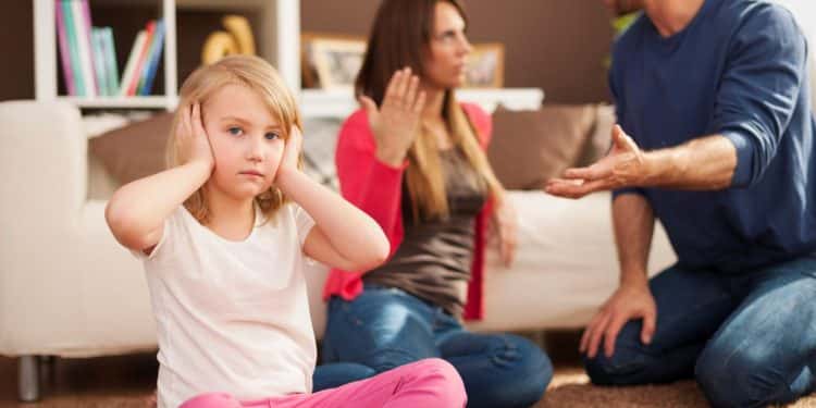 Menina cobre os ouvidos enquanto presencia um desentendimento entre os pais na sala de casa.