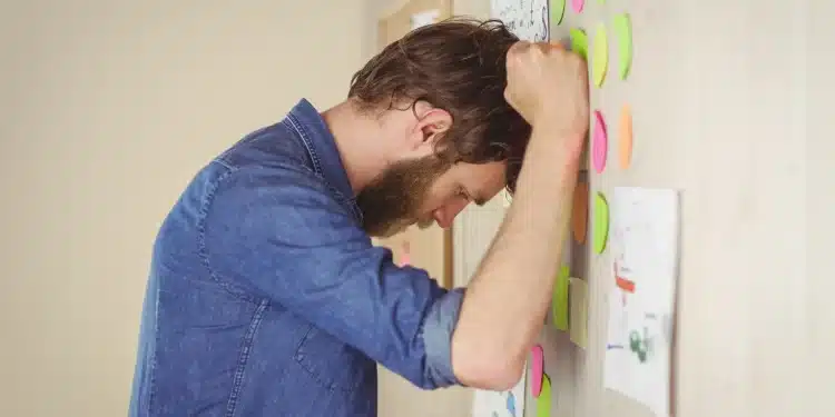 Homem frustrado encostando a cabeça em um mural com post-its coloridos, simbolizando dificuldade em organizar rotinas e controlar impulsos.