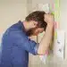 Homem frustrado encostando a cabeça em um mural com post-its coloridos, simbolizando dificuldade em organizar rotinas e controlar impulsos.