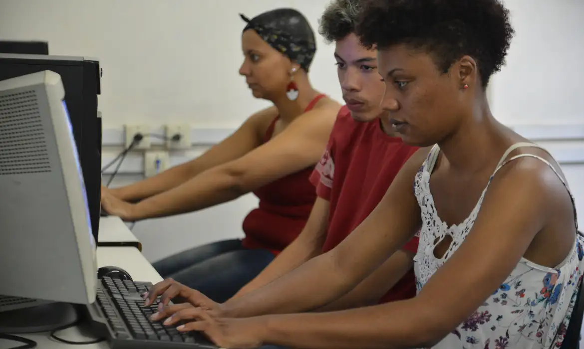 Jovens estudantes concentrados em frente a computadores em sala de aula — formação tecnóloga em áreas de TI e gestão está entre as mais bem pagas em 2026