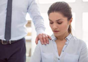 Mulher em ambiente de trabalho sendo tocada no ombro por colega, representando situação de assédio no trabalho.
