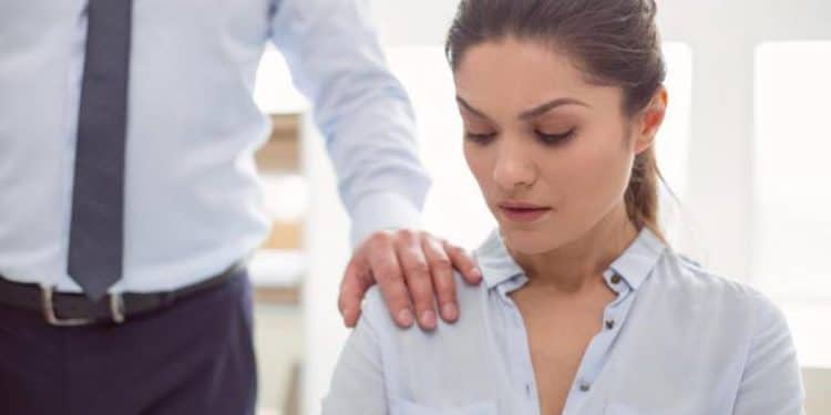 Mulher em ambiente de trabalho sendo tocada no ombro por colega, representando situação de assédio no trabalho.