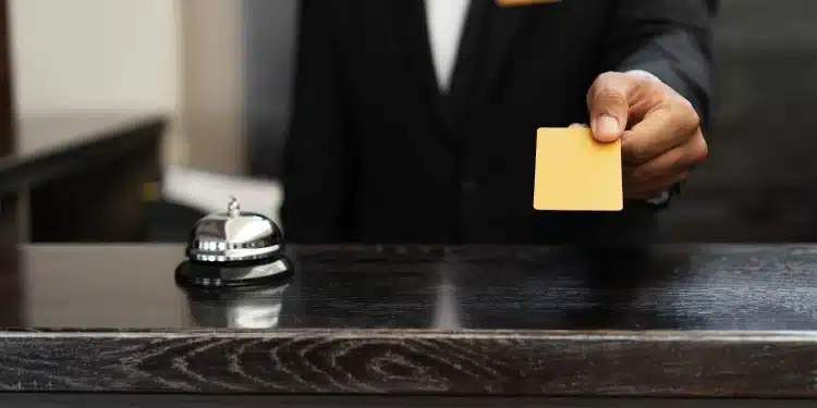 Funcionário de recepção entrega cartão amarelo sobre balcão ao lado de campainha