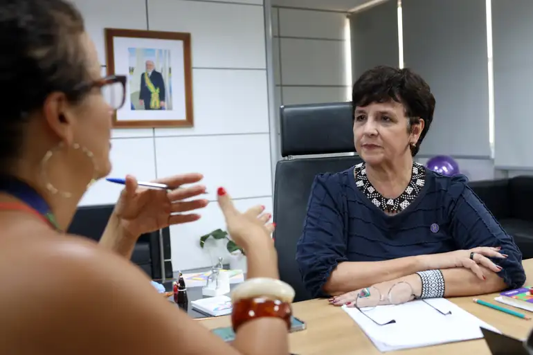 Duas mulheres em reunião profissional em ambiente corporativo, representando uma entrevista de emprego com candidata gesticulando e recrutadora ouvindo atentamente
