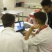 Dois jovens estagiários trabalhando em laptops em uma sala, com um supervisor de jaleco branco orientando, representando o ambiente de estágio profissional e os direitos trabalhistas propostos pelo PL 6350/25