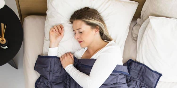 Mulher jovem dormindo tranquilamente em cama com travesseiros brancos e cobertor azul, representando os benefícios de uma boa rotina de sono para a saúde cardiovascular