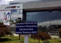 Fachada do edifício sede do Instituto Nacional de Estudos e Pesquisas Educacionais Anísio Teixeira, o INEP, com placa de identificação institucional em azul e branco em primeiro plano e painel comemorativo dos 80 anos do instituto ao fundo, órgão responsável pela organização do Encceja 2026