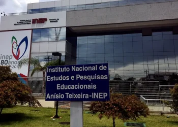 Fachada do edifício sede do Instituto Nacional de Estudos e Pesquisas Educacionais Anísio Teixeira, o INEP, com placa de identificação institucional em azul e branco em primeiro plano e painel comemorativo dos 80 anos do instituto ao fundo, órgão responsável pela organização do Encceja 2026