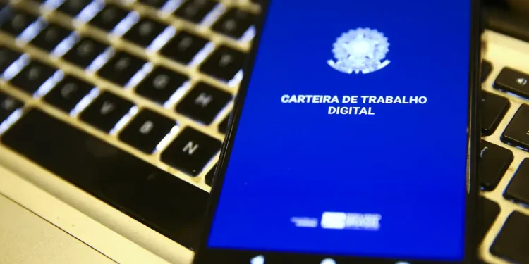 Smartphone exibindo a tela inicial do aplicativo Carteira de Trabalho Digital sobre teclado de notebook, representando o mercado de trabalho em 2026