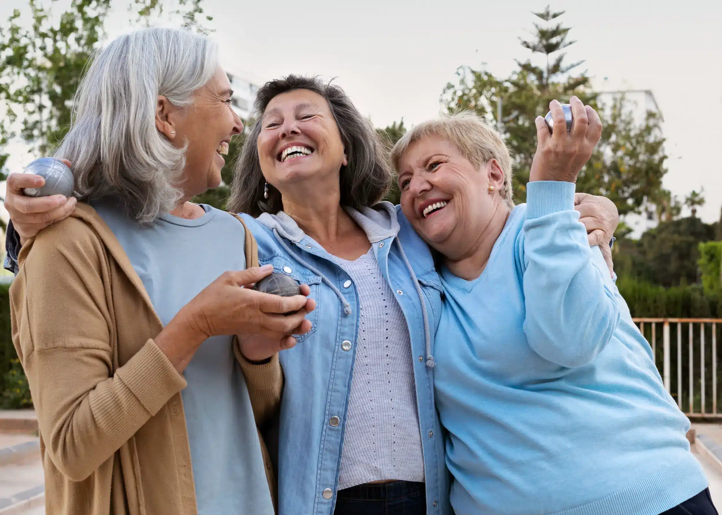 Três mulheres maduras sorrindo e convivendo ao ar livre, representando bem-estar e os aspectos positivos do envelhecimento.