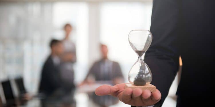 Escala 6x1: executivo segura ampulheta em reunião corporativa, simbolizando o debate sobre jornada de trabalho