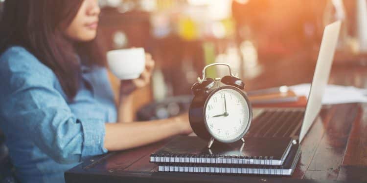 Mulher trabalhando com laptop e relógio analógico em primeiro plano — futuro dos trabalhadores de aplicativos e discussão sobre o fim da escala 6x1