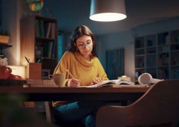 Mulher estudando sozinha à noite, com livros e uma xícara de café na mesa. Imagem que simboliza a dedicação ao estudo para o Enem.