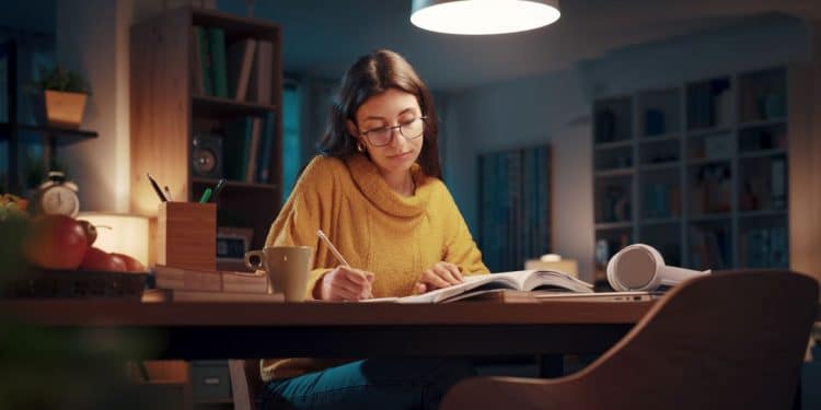 Mulher estudando sozinha à noite, com livros e uma xícara de café na mesa. Imagem que simboliza a dedicação ao estudo para o Enem.