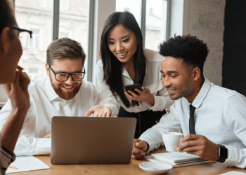 olegas de trabalho sorrindo e colaborando em equipe em frente a um computador, ilustrando a regra dos três metros e o bem-estar profissional.