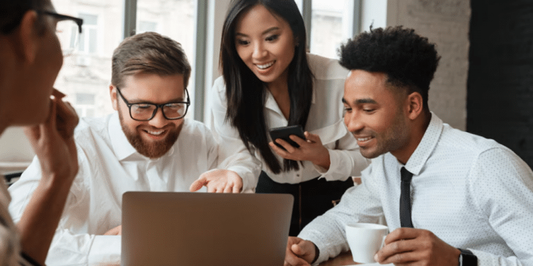 olegas de trabalho sorrindo e colaborando em equipe em frente a um computador, ilustrando a regra dos três metros e o bem-estar profissional.