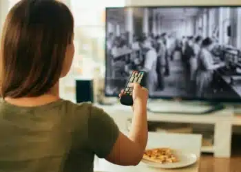 Mulher assistindo a filme sobre a Revolução Industrial, com foco em trabalhadores operando máquinas.