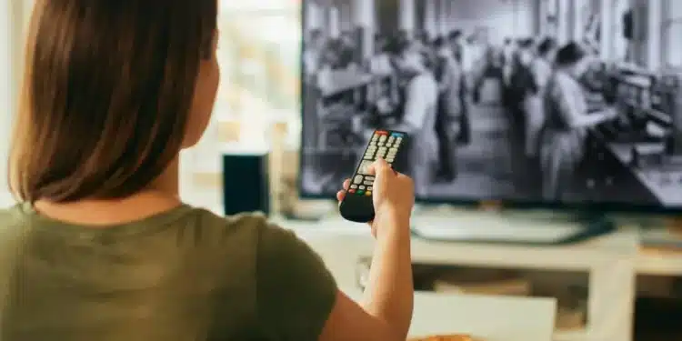 Mulher assistindo a filme sobre a Revolução Industrial, com foco em trabalhadores operando máquinas.