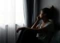 Mulher sentada perto da janela olhando para fora em momento de reflexão emocional e introspecção.