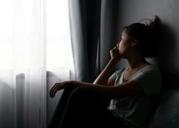 Mulher sentada perto da janela olhando para fora em momento de reflexão emocional e introspecção.