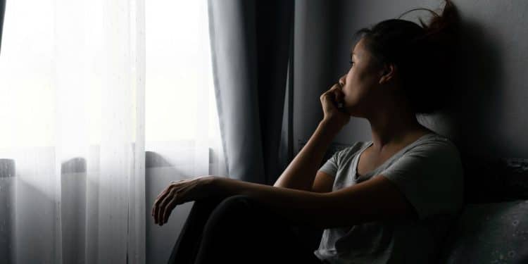 Mulher sentada perto da janela olhando para fora em momento de reflexão emocional e introspecção.