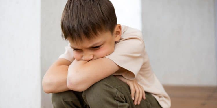 Menino triste sentado, refletindo sobre o impacto das palavras no desenvolvimento emocional infantil.