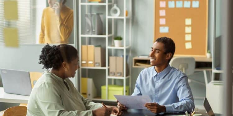 Dois profissionais conversam e analisam documentos durante reunião de trabalho em escritório.