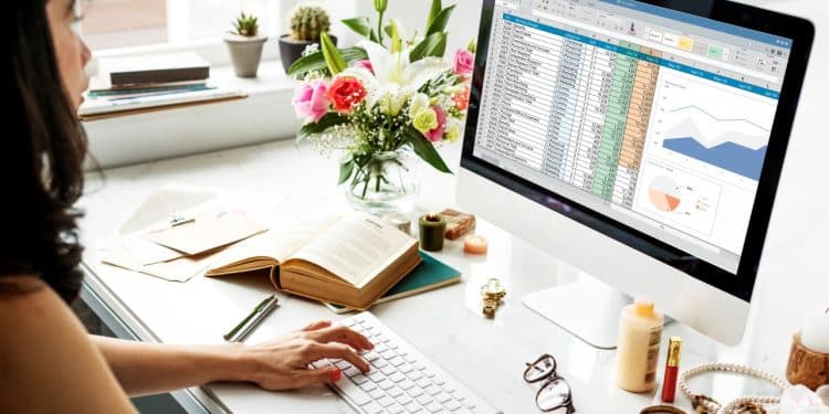 Mulher trabalhando no computador com planilha do Excel aberta exibindo gráficos e dados financeiros.