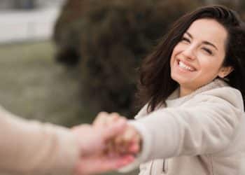 Mulher sorrindo ao segurar a mão de um homem ao ar livre, transmitindo felicidade e confiança.