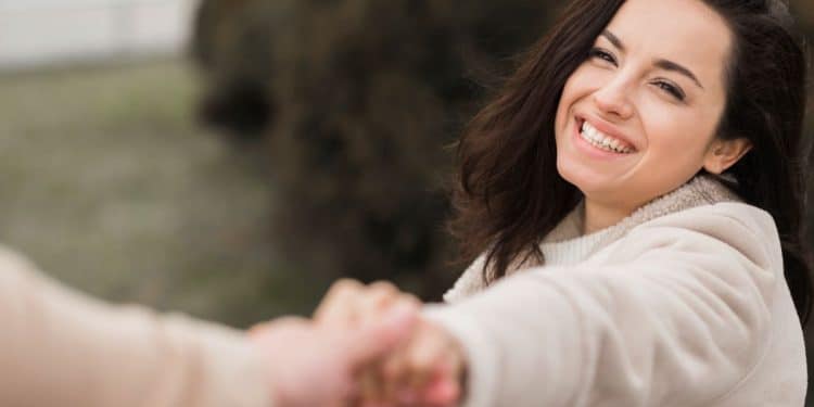 Mulher sorrindo ao segurar a mão de um homem ao ar livre, transmitindo felicidade e confiança.