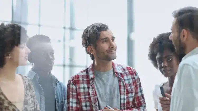 Quatro pessoas em pé conversando e ouvindo atentamente em ambiente corporativo iluminado