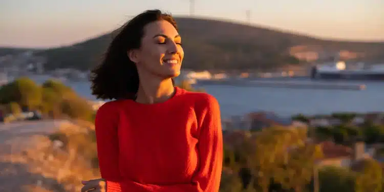 Mulher sorrindo ao ar livre durante o pôr do sol representando hábitos positivos para uma vida mais equilibrada.