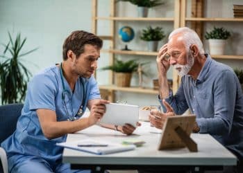 Enfermeiro homem mostra tablet para paciente idoso em consulta — homens em profissões de cuidado