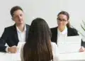 Candidata de costas sendo entrevistada por dois recrutadores em ambiente corporativo, representando o momento da entrevista de emprego para o qual a Inteligência Artificial pode ajudar na preparação