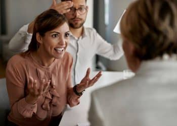 Mulher em uma discussão intensa com agente imobiliário durante reunião, mostrando sinais de manipulação emocional.