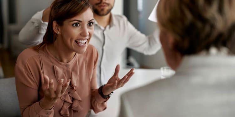 Mulher em uma discussão intensa com agente imobiliário durante reunião, mostrando sinais de manipulação emocional.